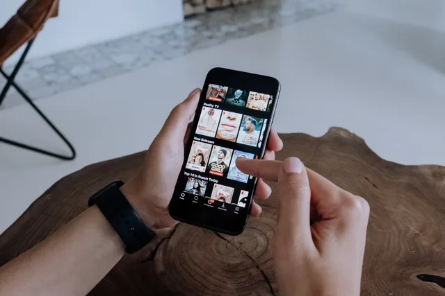 A person using a smartphone to explore and select shows on a streaming platform indoors. Reducing avoidable subscription churn