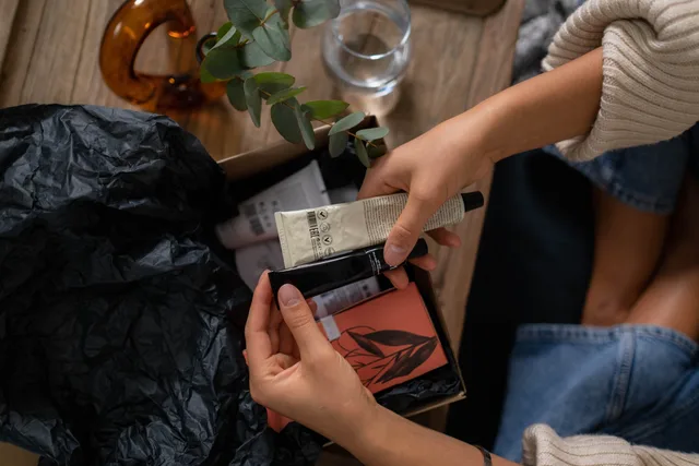 Hands unboxing skincare products with eucalyptus on wooden surface. Subscription commerce for physical products